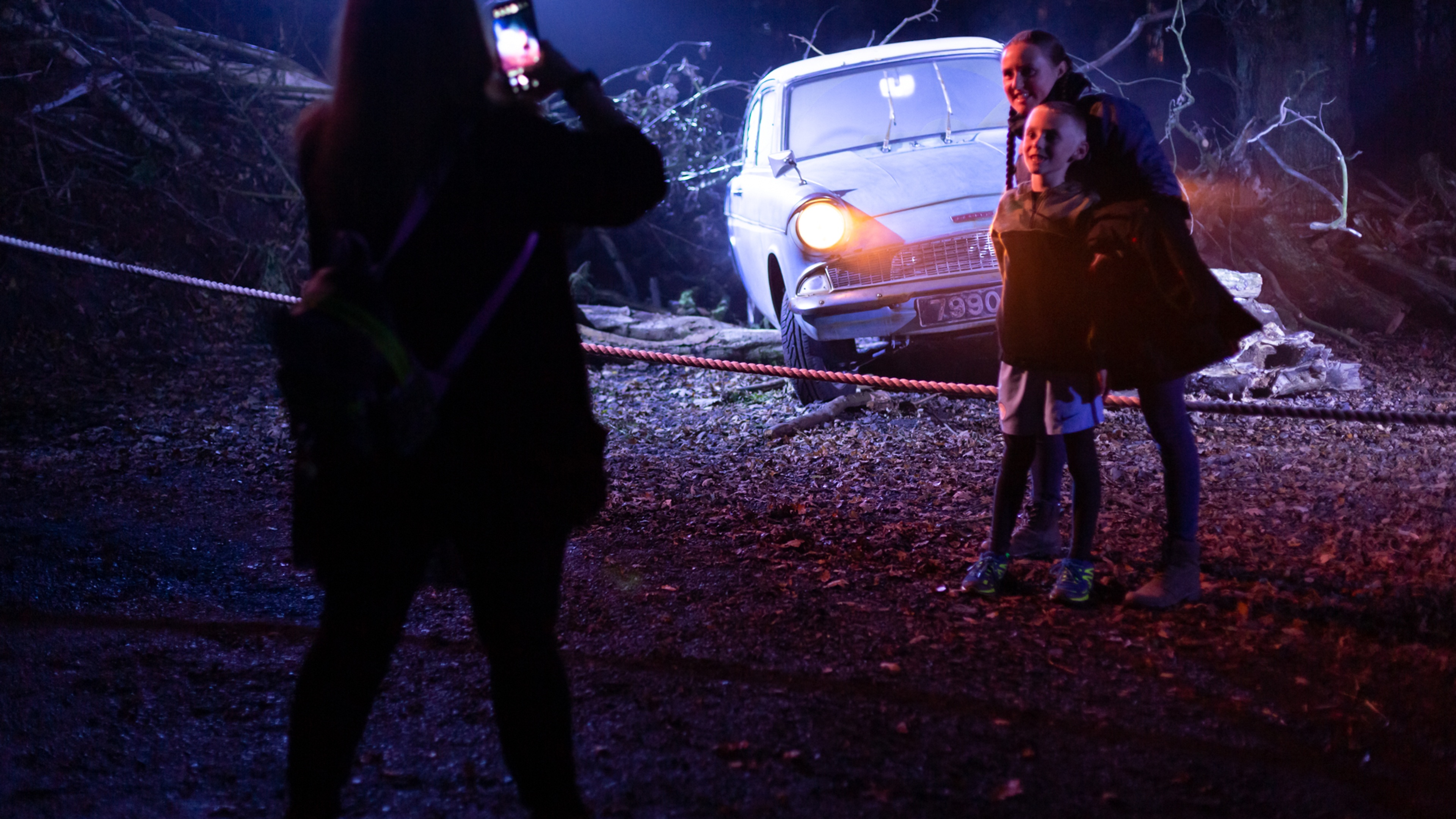 Harry Potter: A Forbidden Forest Experience Woman taking photo of a girl and teenager in front of a car with the headlights on