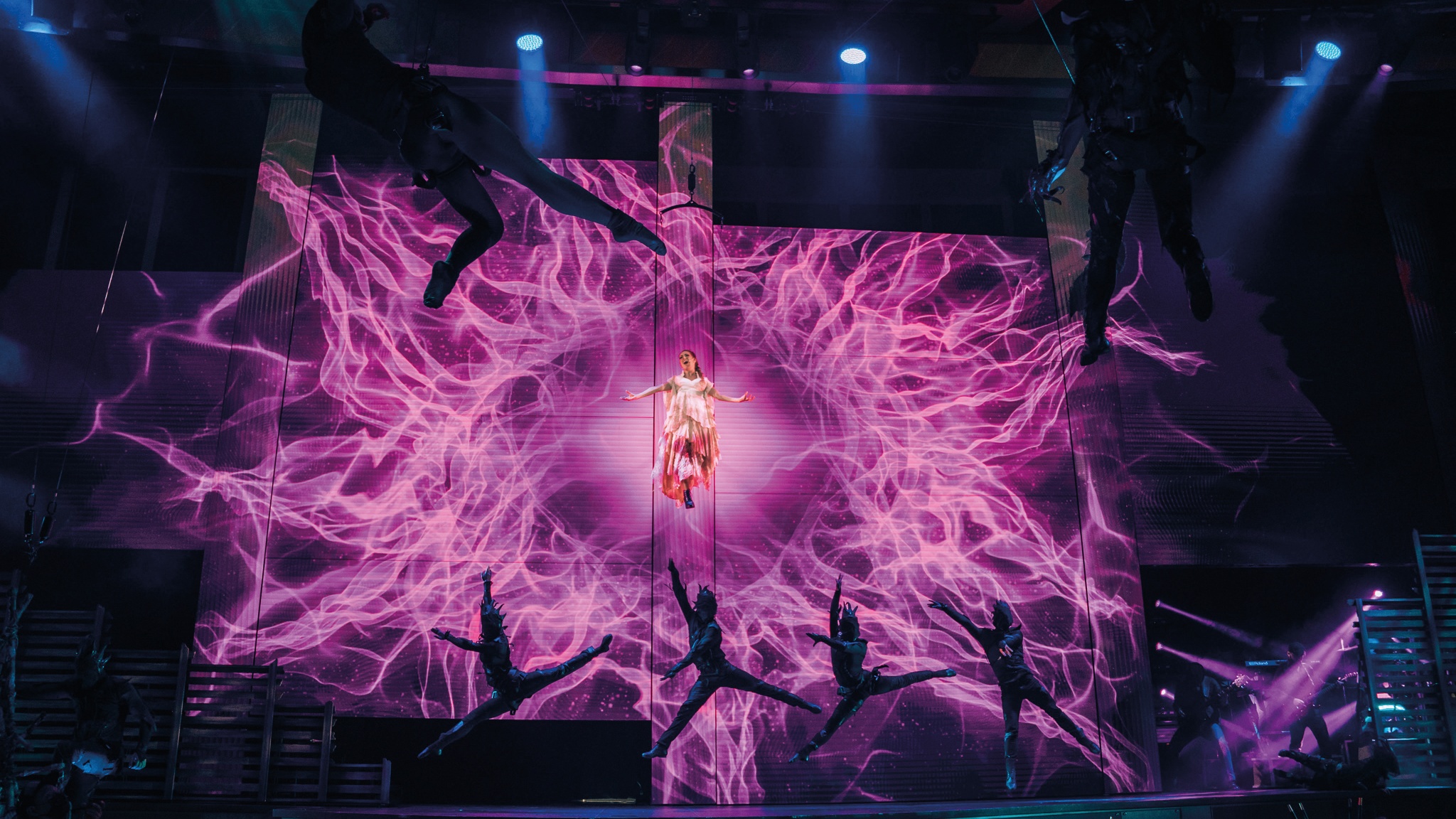 Carnival Cruise Line Mardi Gras silhouettes of dancers performing, while flying perform sings in front of an abstract pink animation