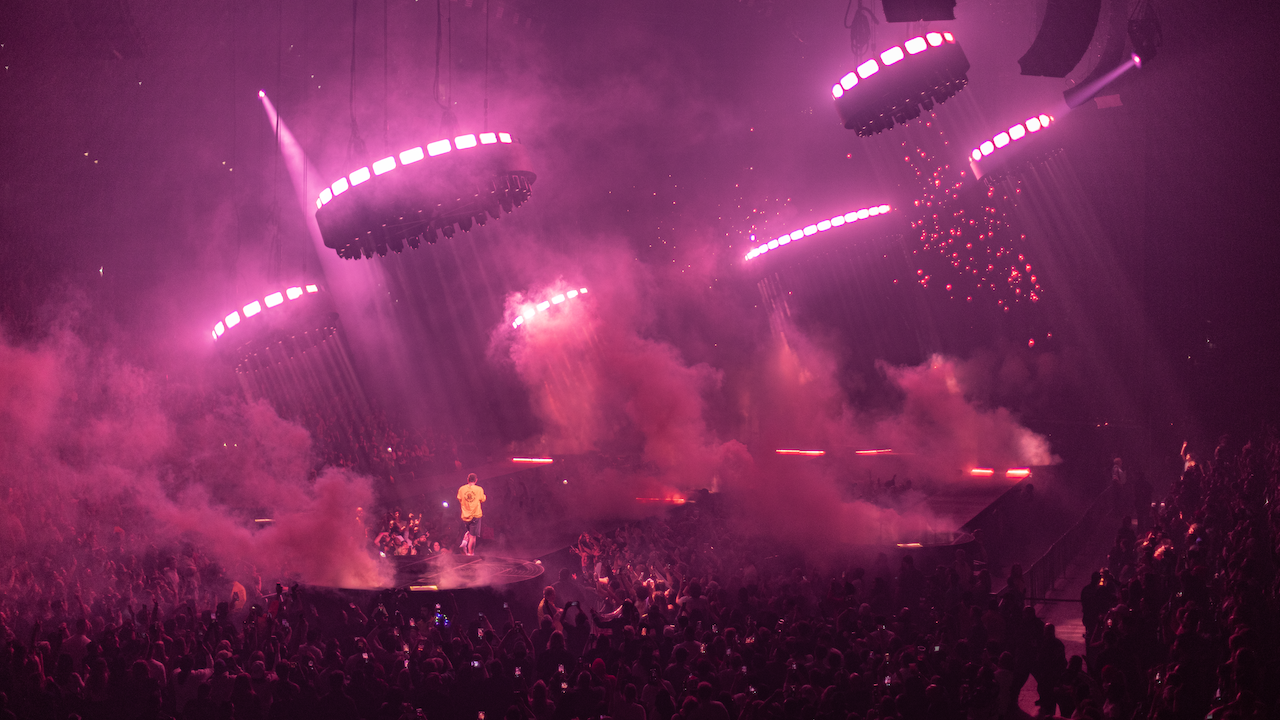 Post Malone performing on stage in yellow shirt with pink overhead lighting