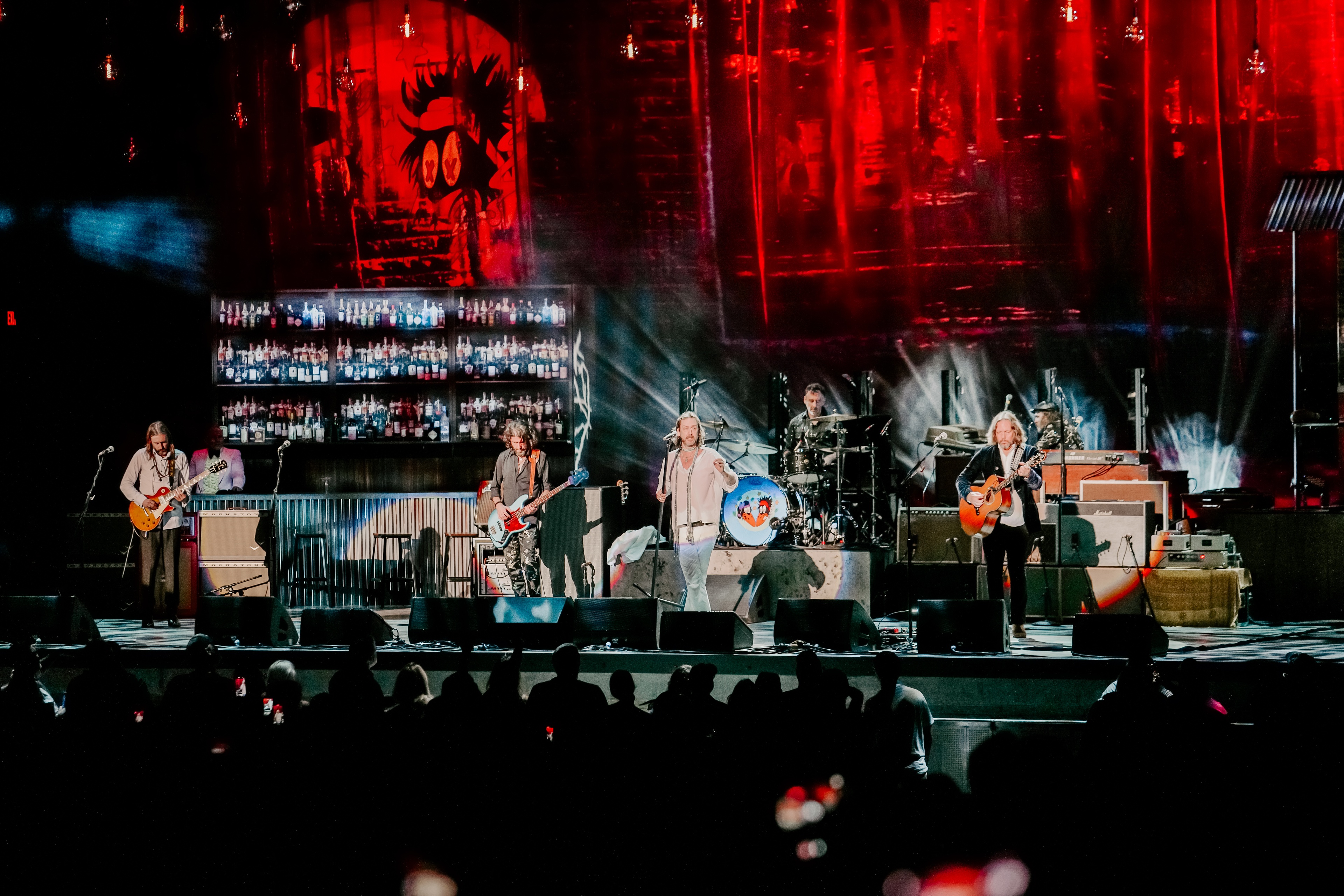 silhouettes of crowd watching the Black Crowes perform on stage during their Shake Your Money Maker Tour, gritty red lit brick textural wall with graffiti on the backdrop