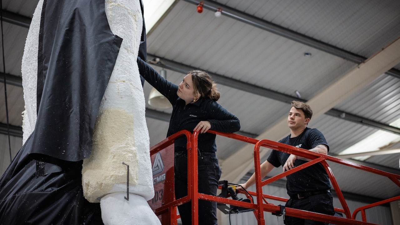 Man and woman on lift dressing a huge polystyrene sculpture of man