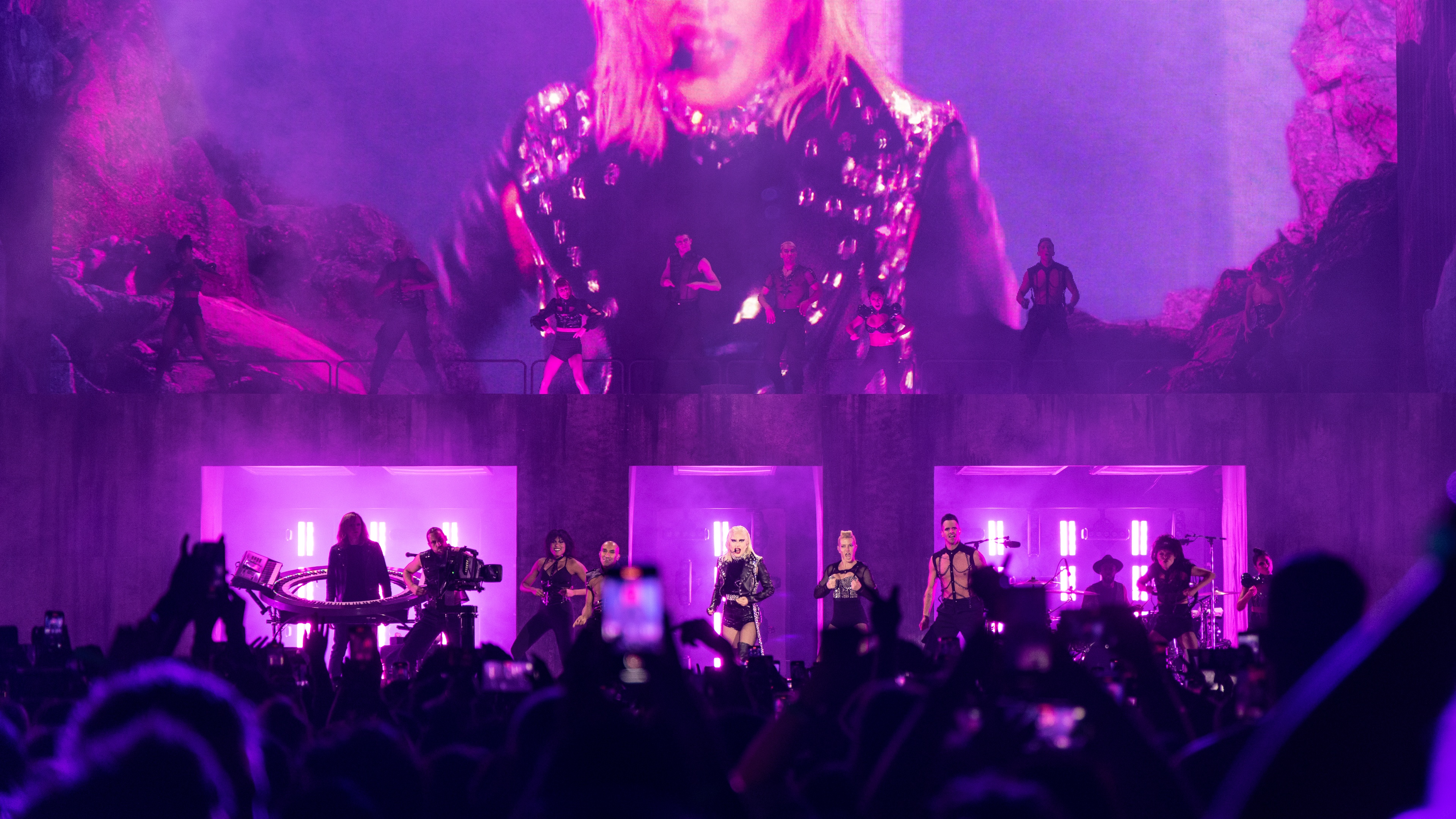Singer Lady Gaga performing on stage with backing dancers in front of pink lighting and huge LED screen of her performing