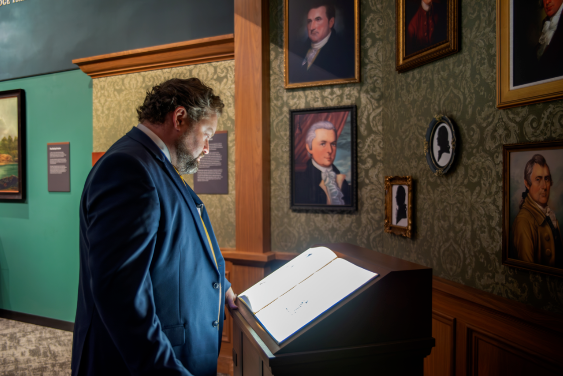 A museum-goer enjoying an interactive digital book surrounded by walls covered in US Presidential portraits