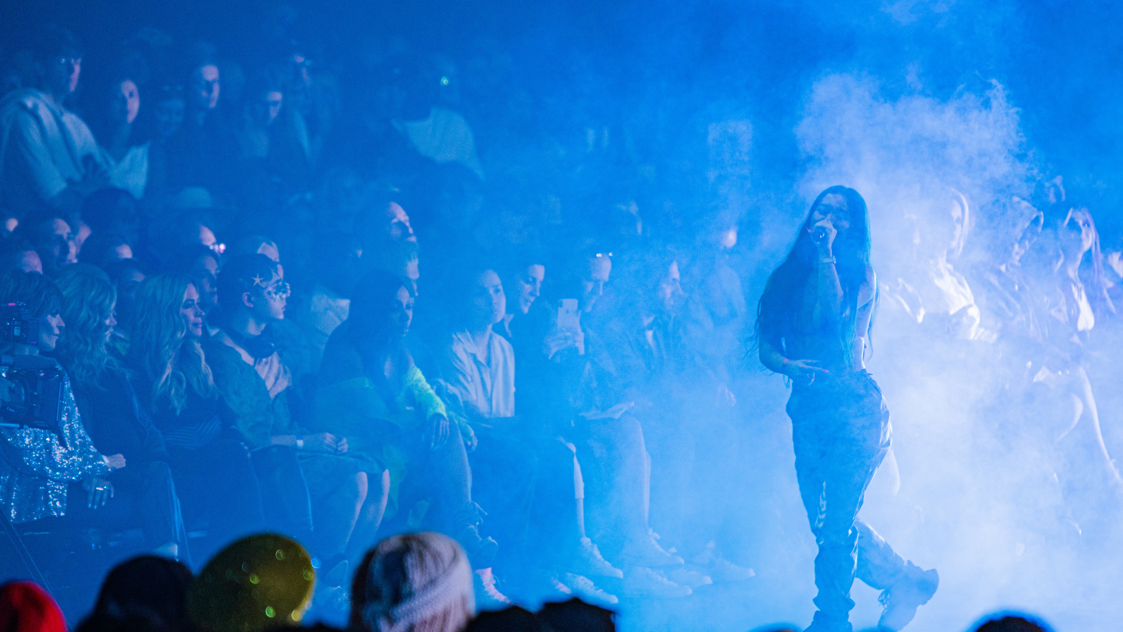 Woman with long black hair performing in front of crowd with blue lights
