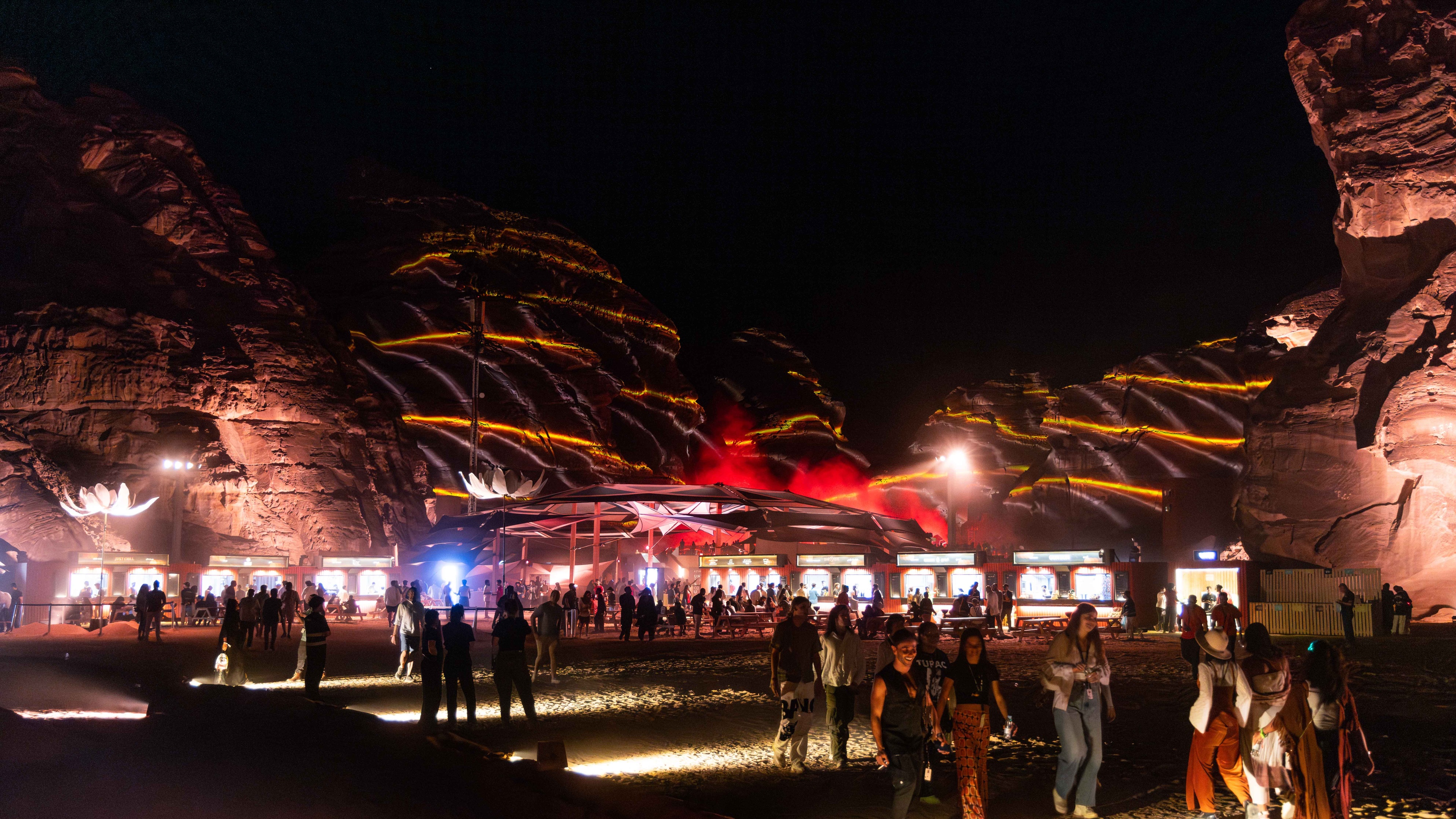 Crowd of people walking between rocky mountains at a festival with spotlights