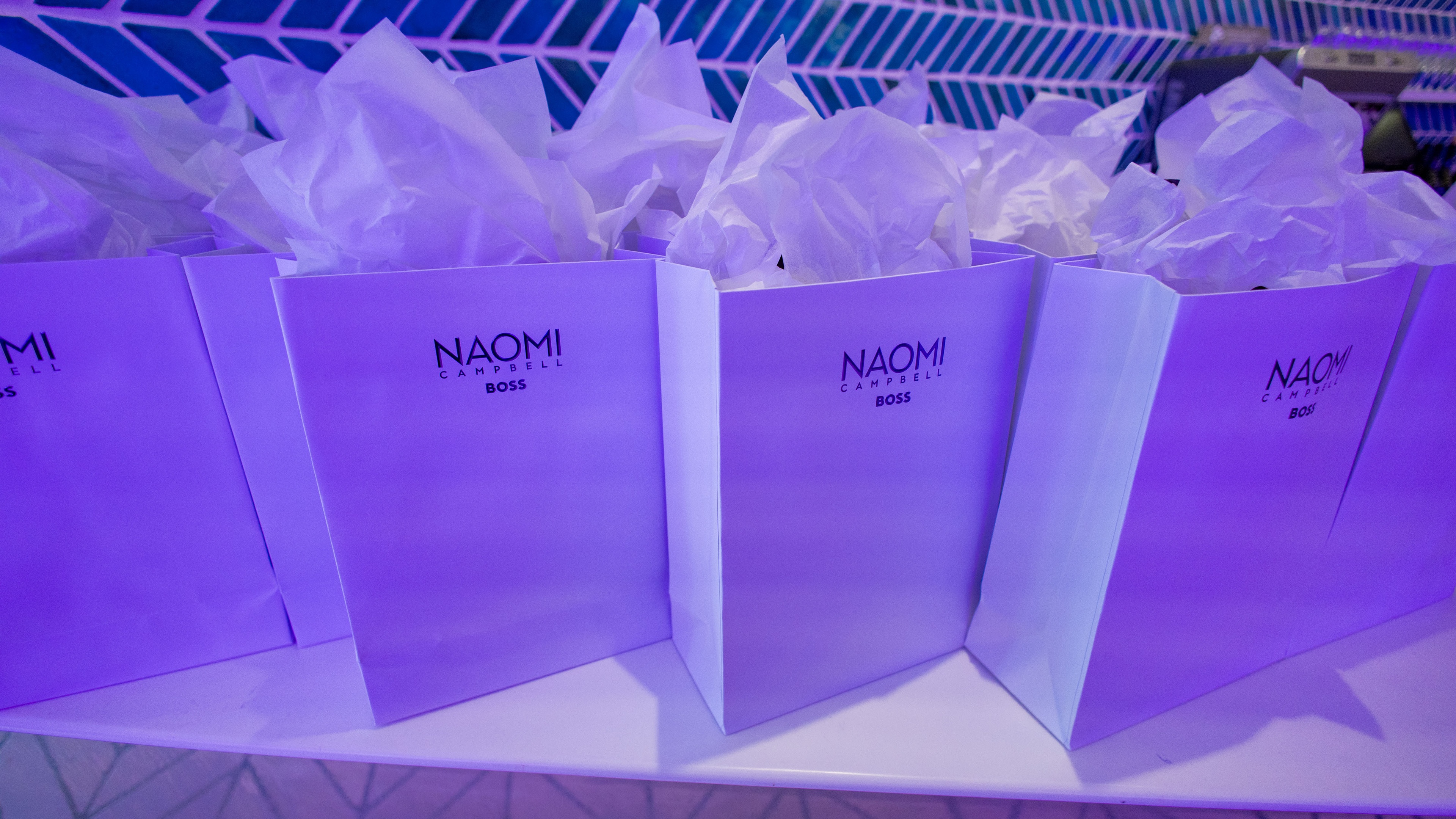 White gift bags lined up with Naomi on front