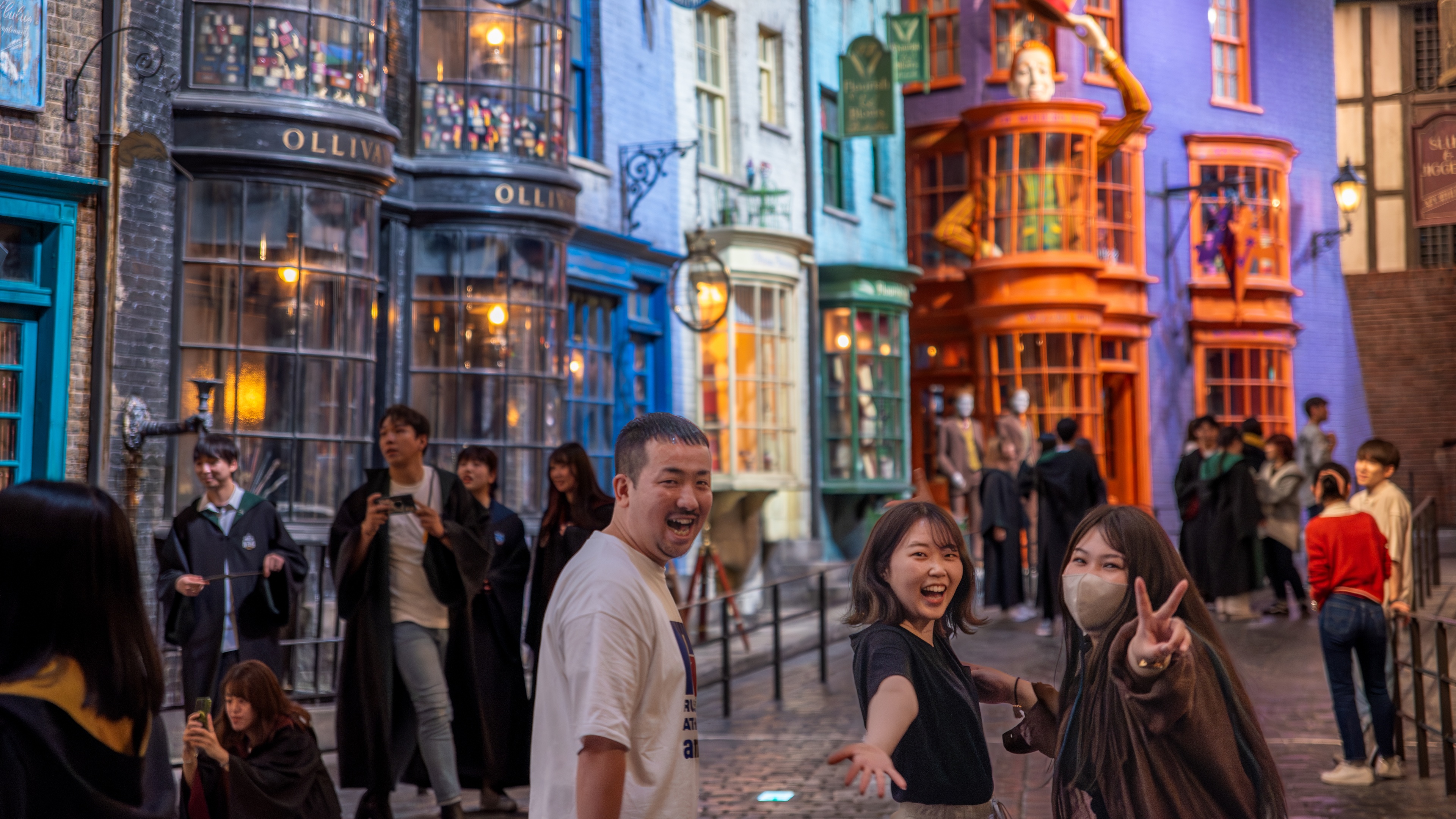 People looking back laughing walking down Diagon Alley showing the peace sign with a crowd in the background