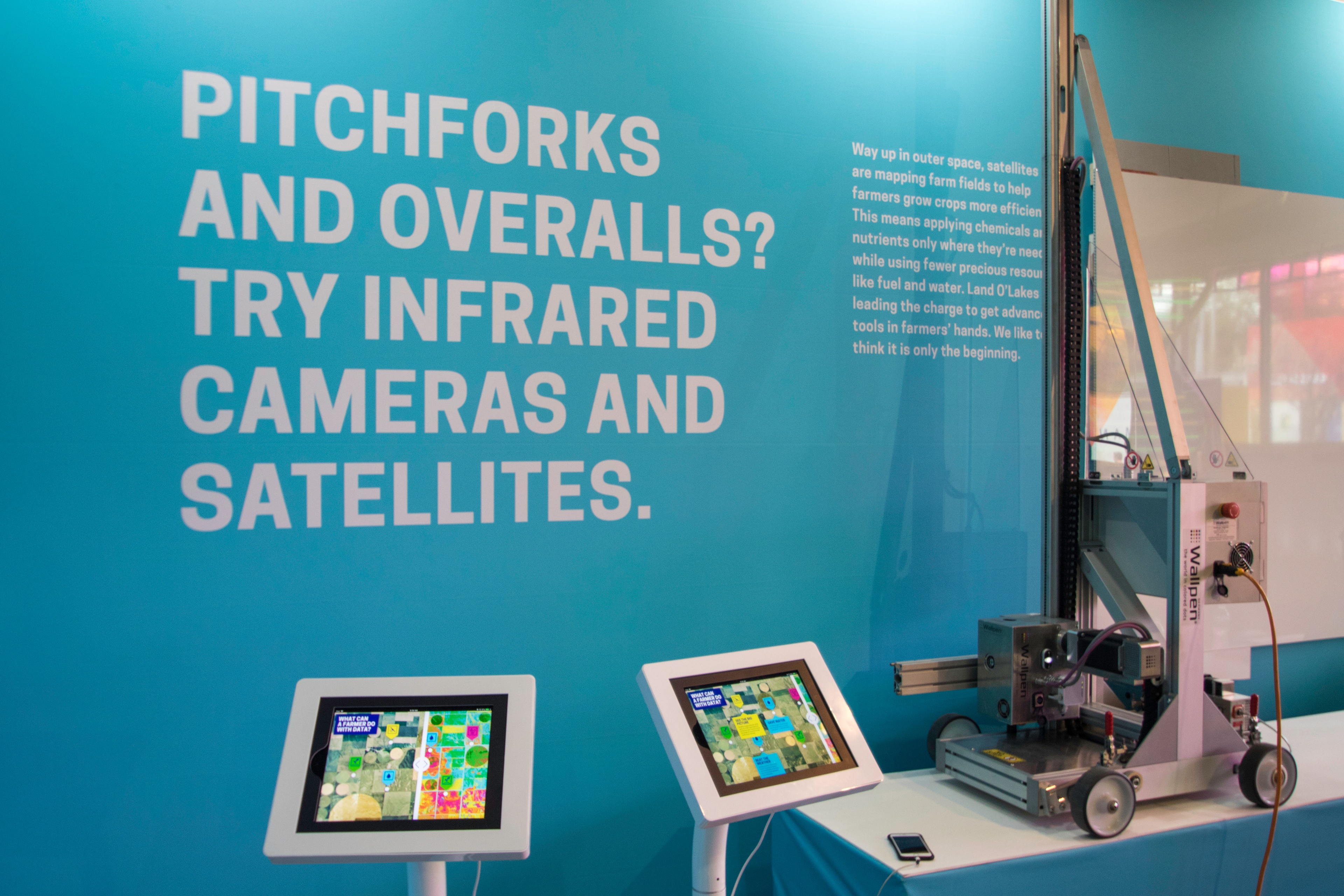 Land O’Lakes The Food Effect SXSW wall with title that reads "PITCHFORKS AND OVERALLS? TRY INFRARED CAMERAS AND SATELLITES." and surrounded by screens and machinery
