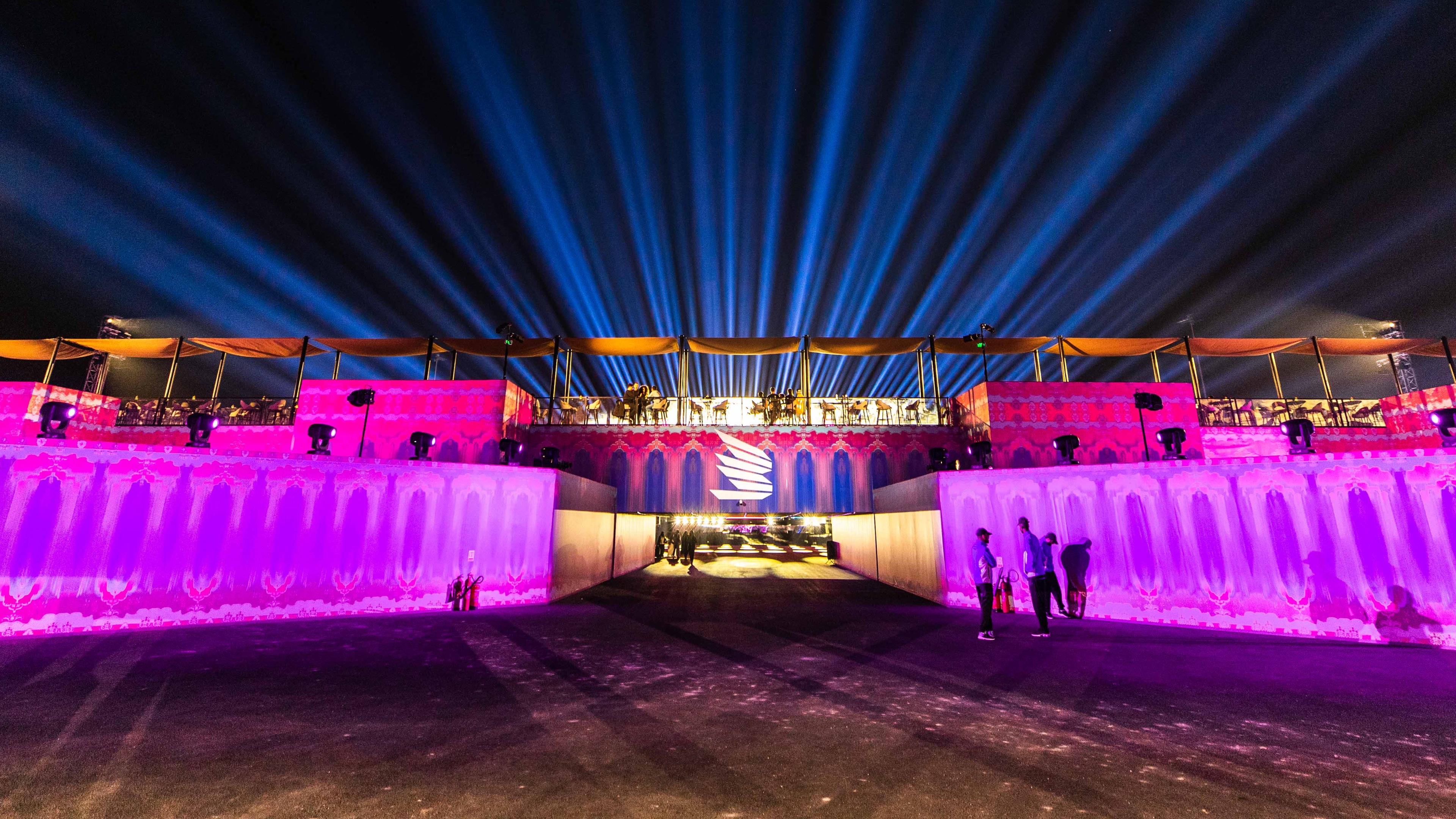 Aravia MDLBEAST entrance lit up in bright pink, bright blue lights in the background, balconies with palm tress