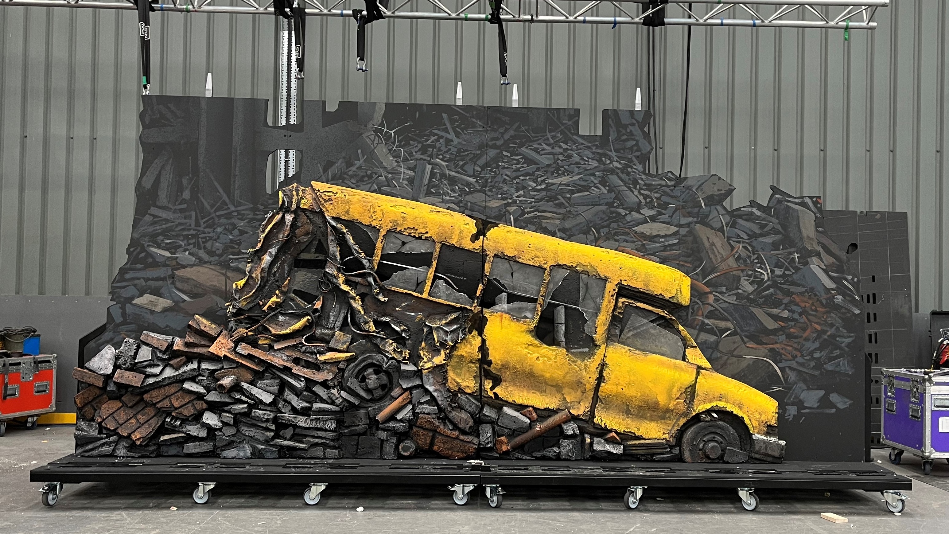 behind the scenes of My Chemical Romance Foundations Tour featuring stage scenery build of a small yellow school bus at an angle falling apart and surround by debris