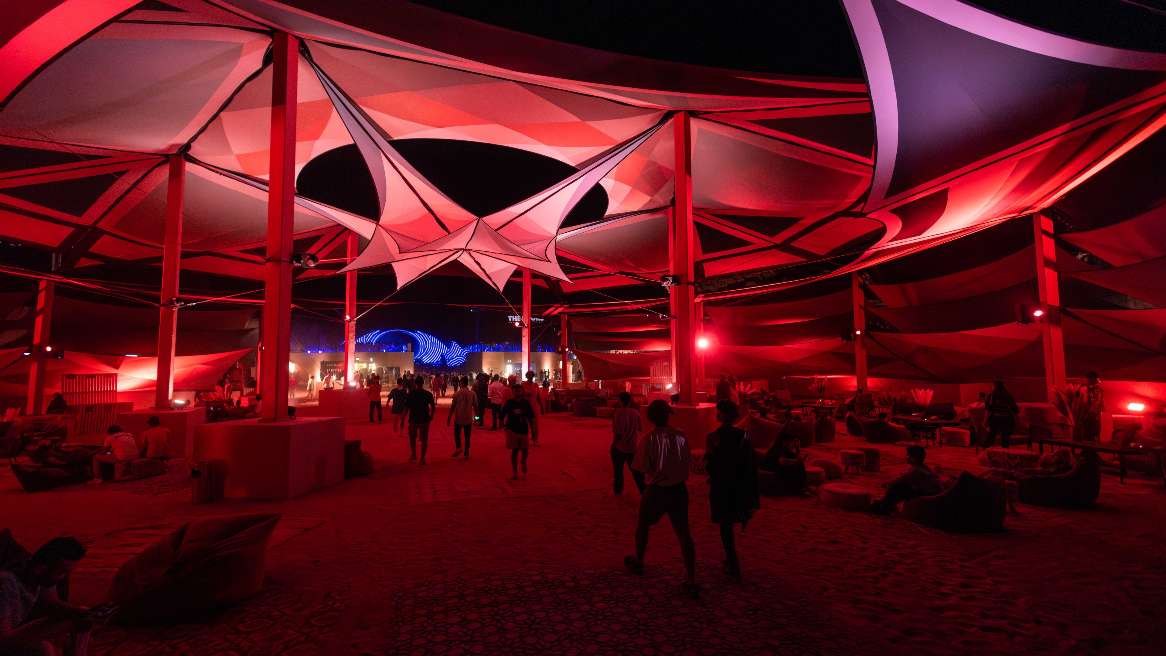 People walking underneath geometric structure with red lighting at night