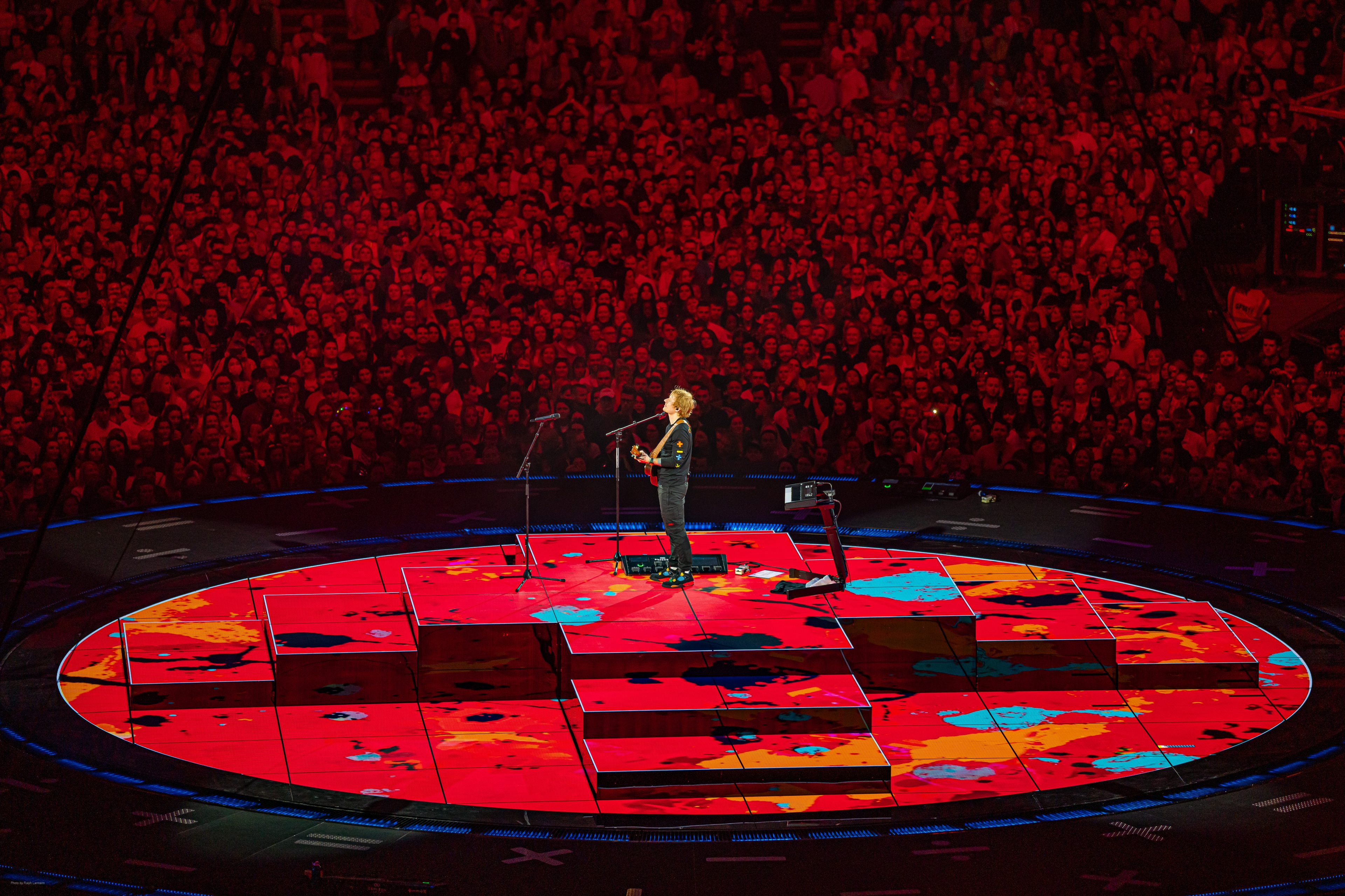 Ed Sheeran playing guitar and singing in center of round LED stage lit up red