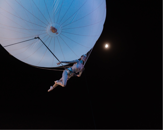 close up of aerial performer floating under a large lit up balloon