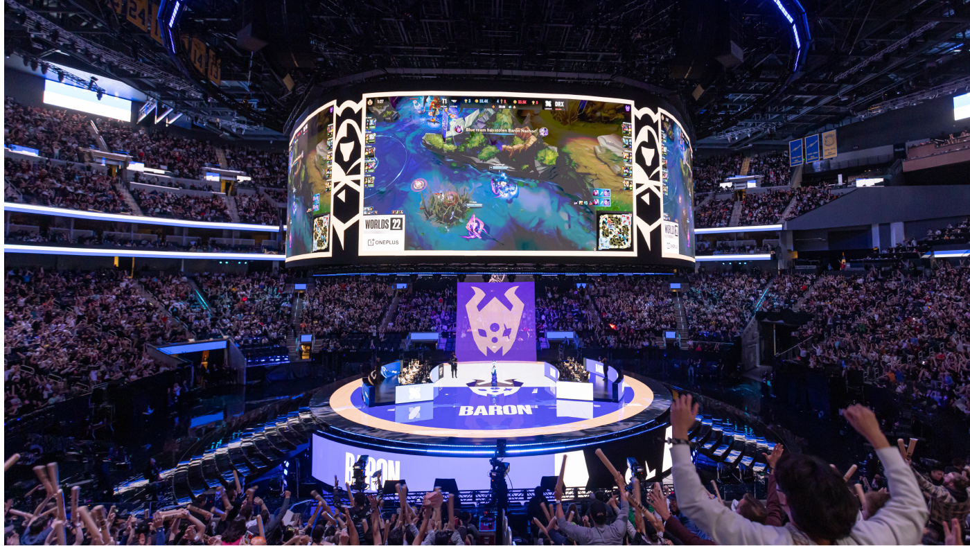audience surrounding a center stage of players competing with large screens displaying the game above