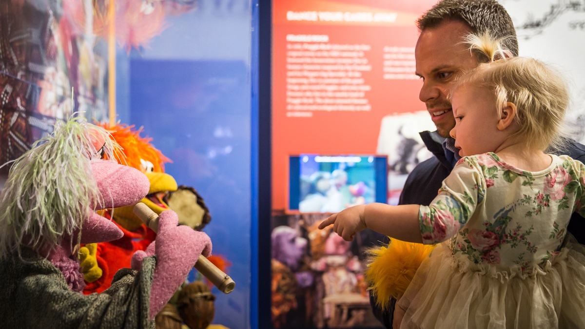 Man holding little girl while pointing at puppet display