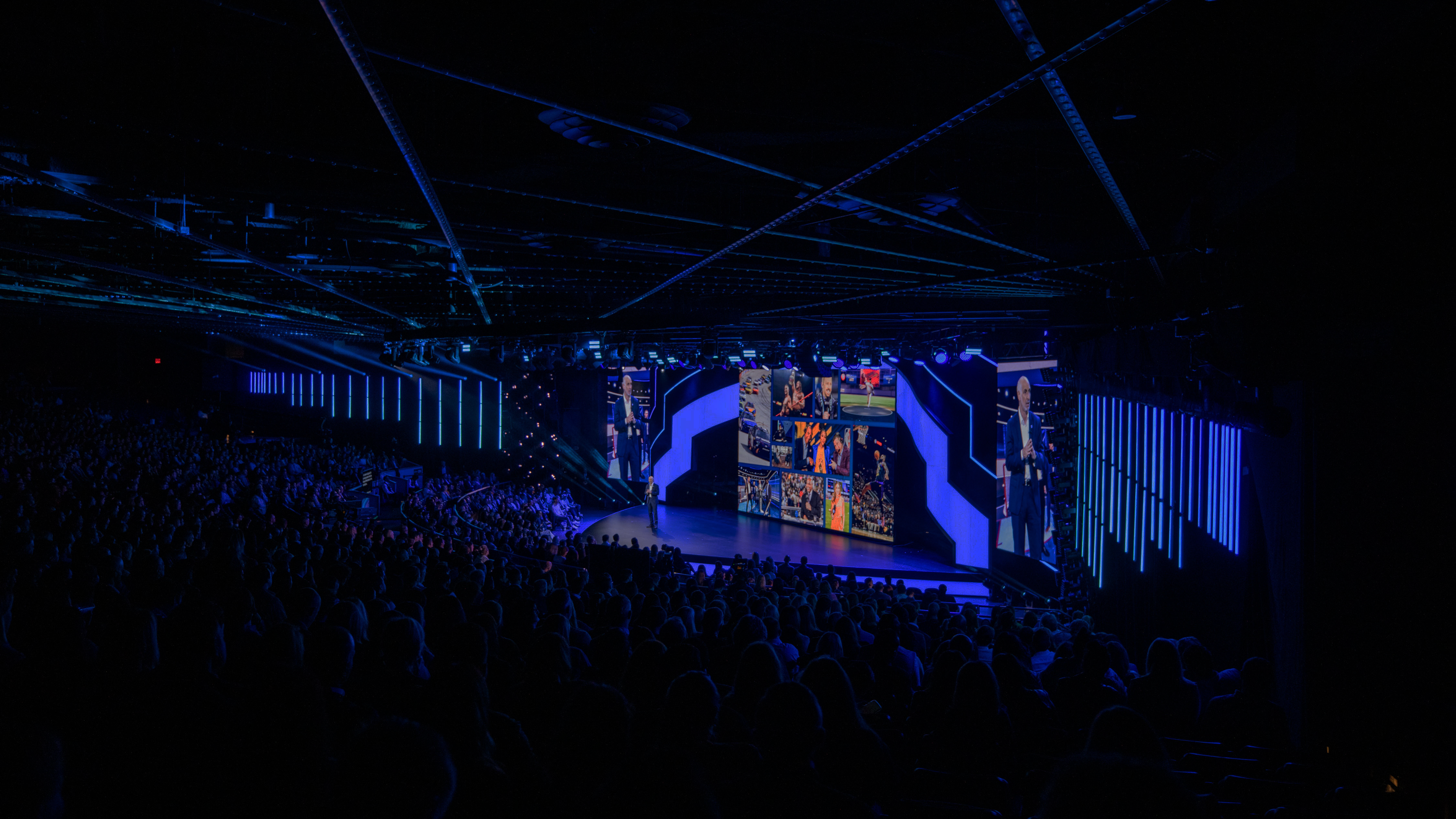 Person standing on stage with blue lights and LED wall