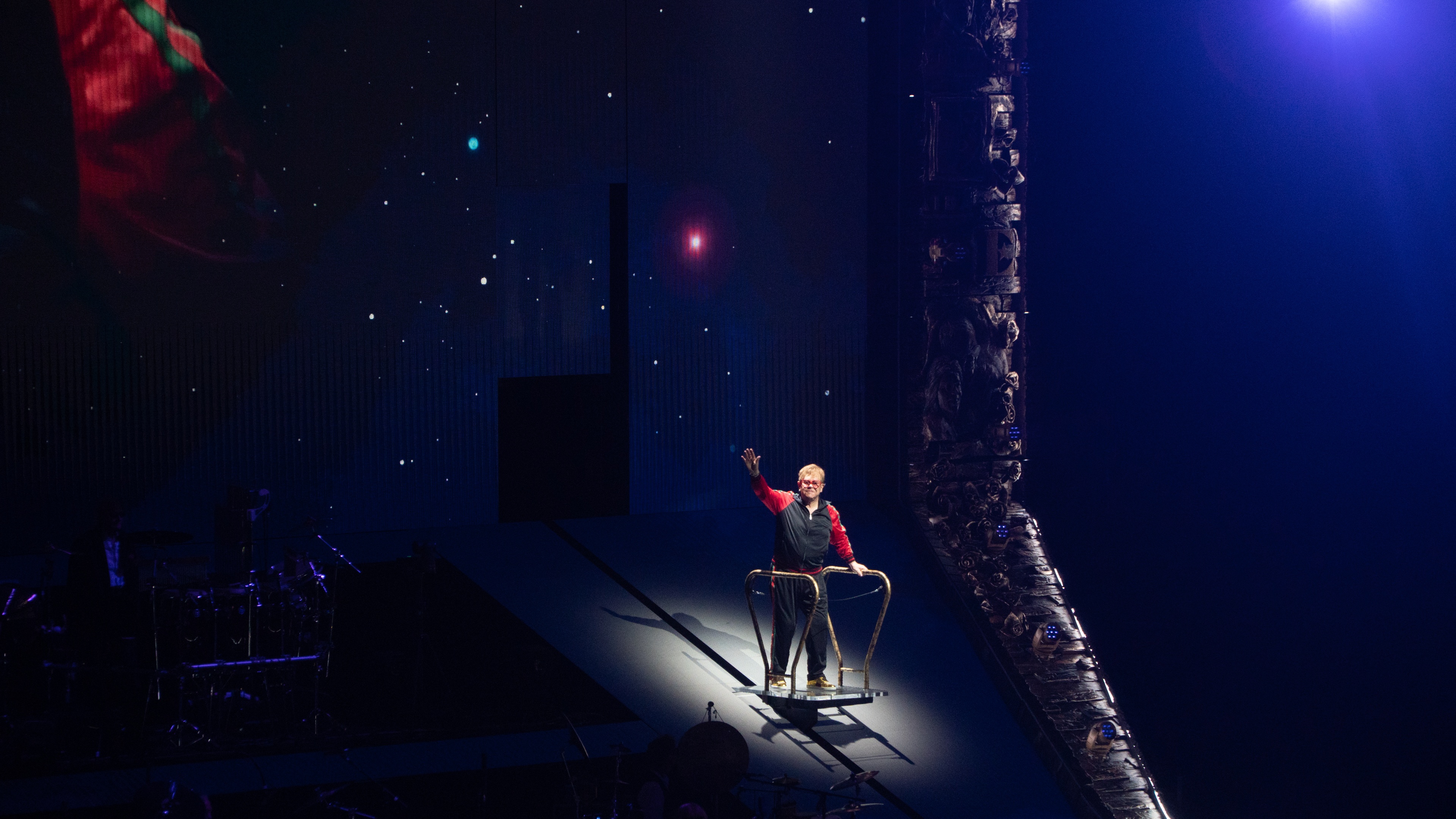 Elton John waving to crow on stage with blue lighting