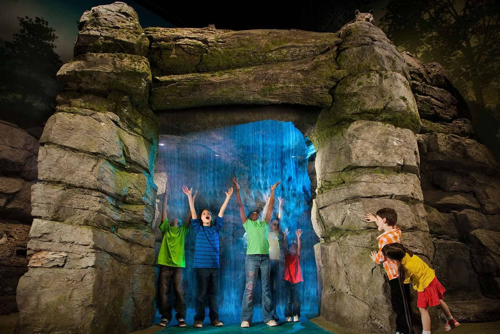 Kids standing under waterfall with arms up cheering