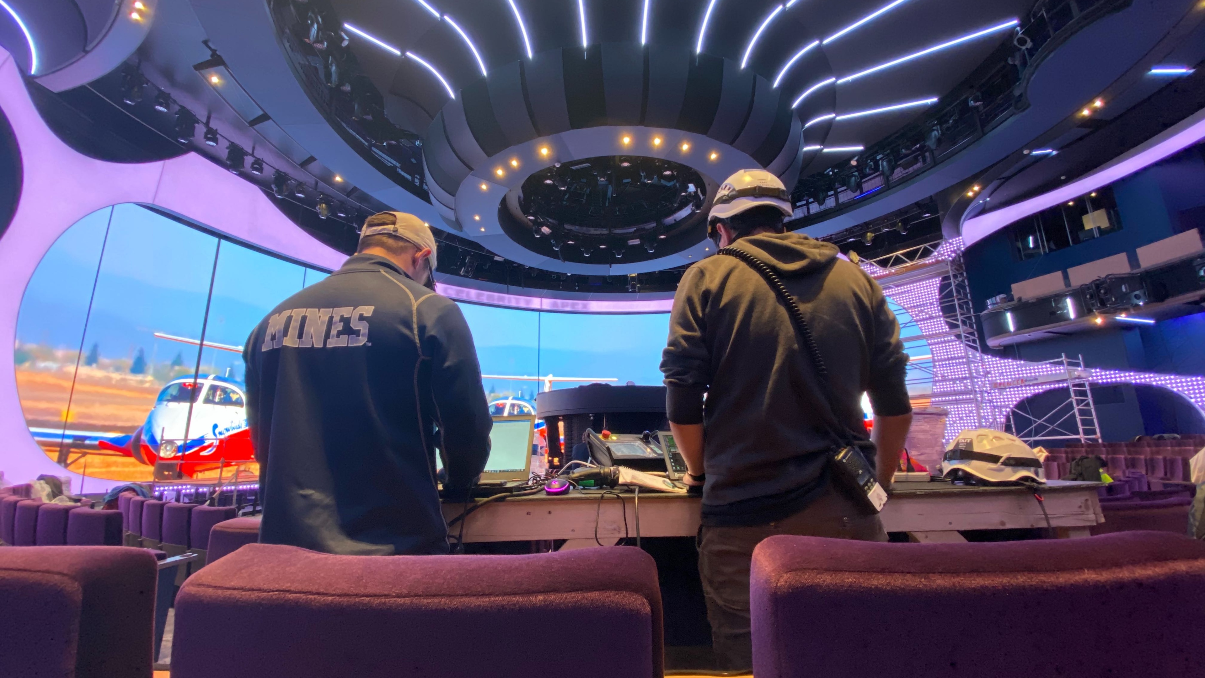 2 workers looking at computer screens in front of giant LED screen and centrepiece sculpture