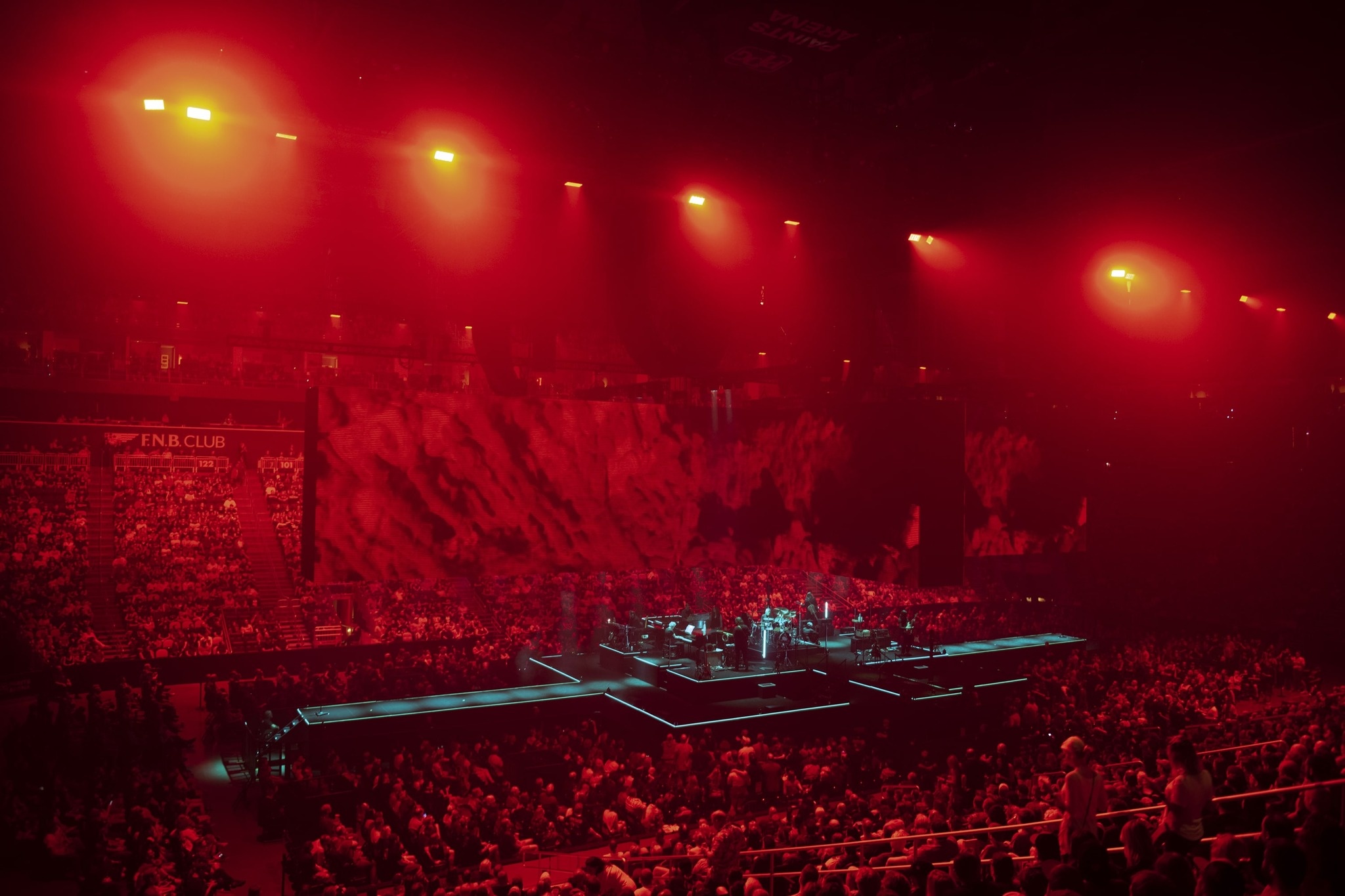 view from the balcony stand of Roger Waters performing during the This Is Not A Drill Tour, red environment, turquoise lights on stage