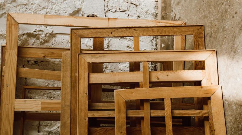 Empty wooden picture frames in varying sizes leaning against a whitewashed brick wall, ready to become a tack room gallery wall