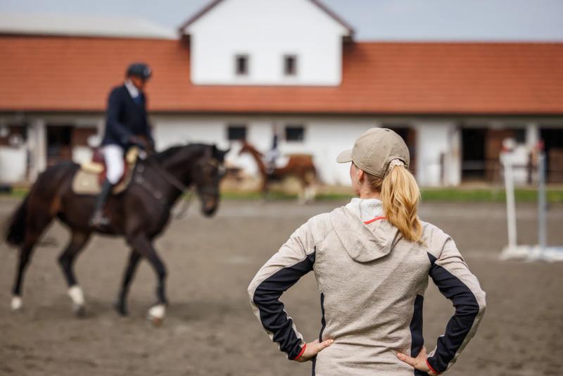 A riding instructor teaching a mounted rider in an arena