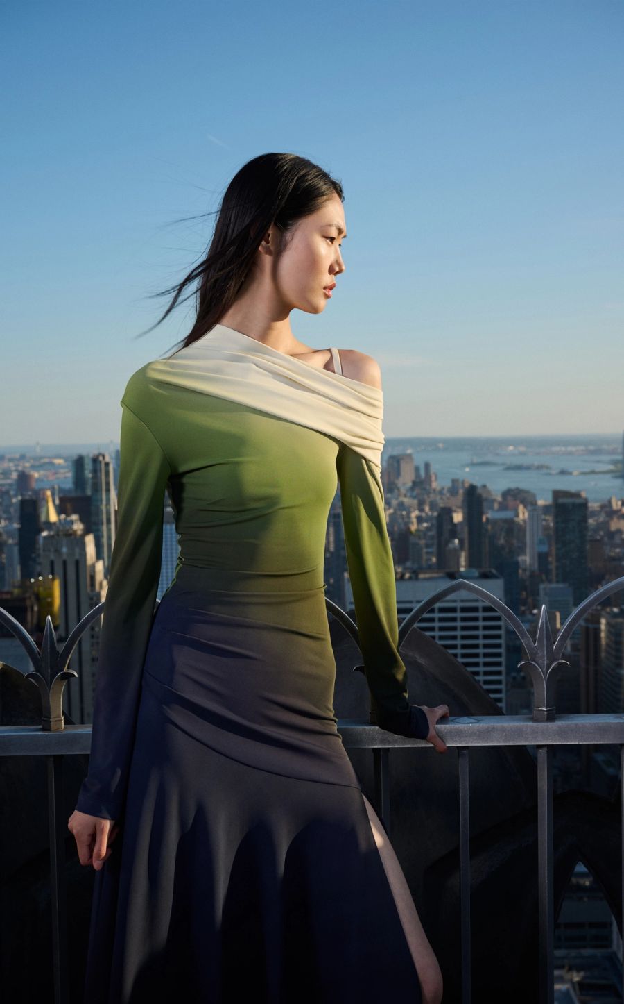 Model in a long green and blue gown with the New York skyline behind