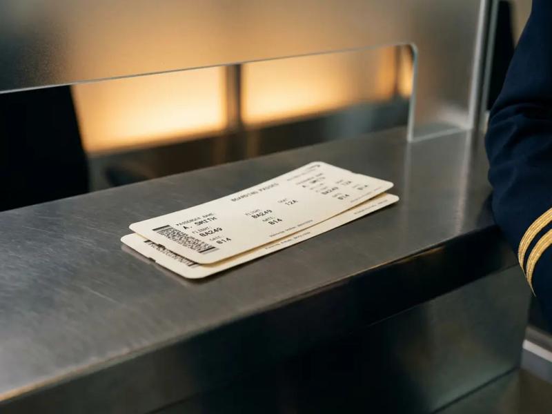 Two identical boarding passes overlapping on an airport check-in desk, with a crew member's navy sleeve visible at the edge.