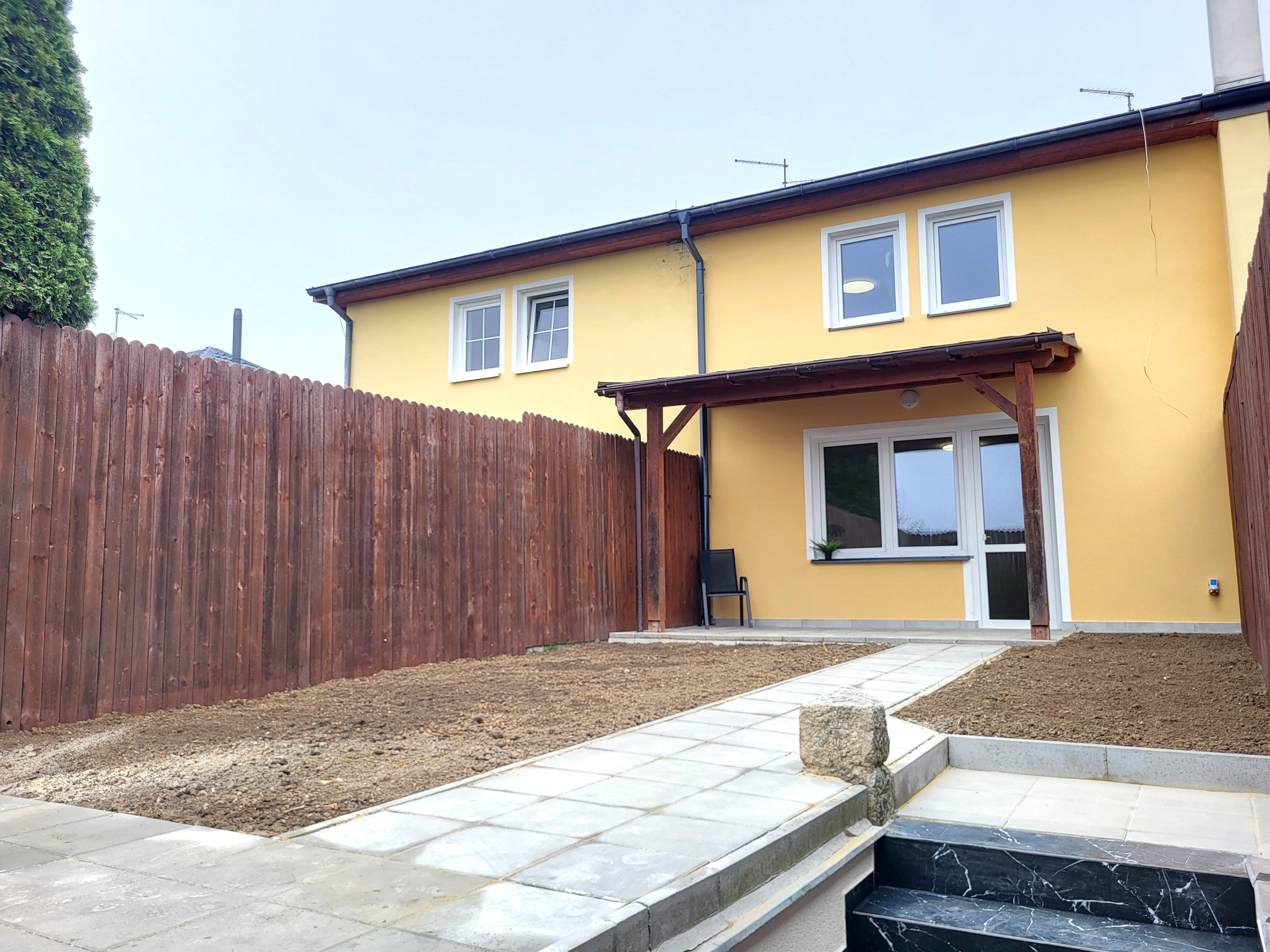 Žlutý řadový dům se zadní terasou a upravovanou zahradou u dřevěného plotu