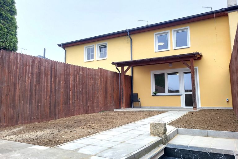 Žlutý řadový dům se zadní terasou a upravovanou zahradou u dřevěného plotu