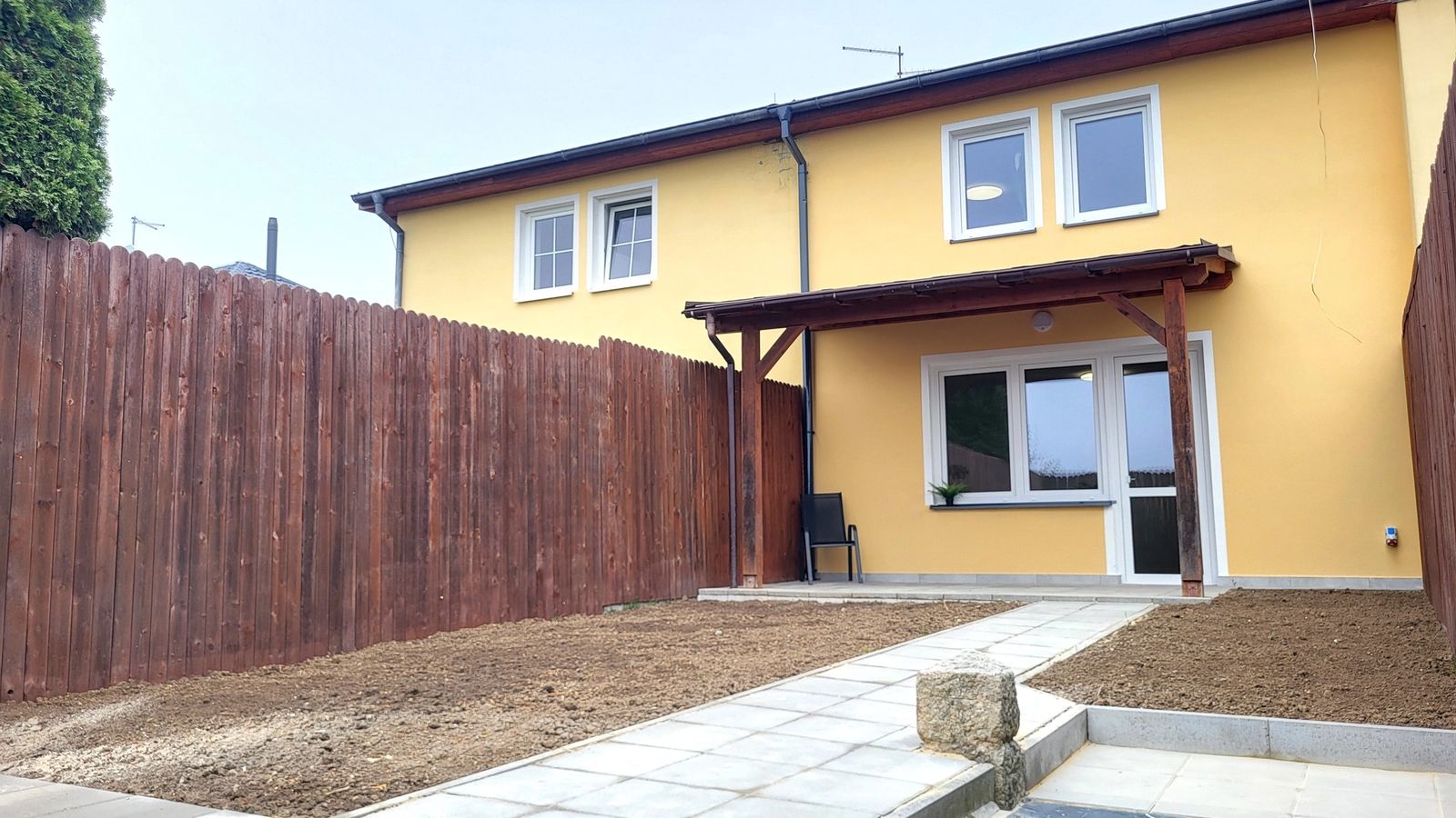 Žlutý řadový dům se zadní terasou a upravovanou zahradou u dřevěného plotu
