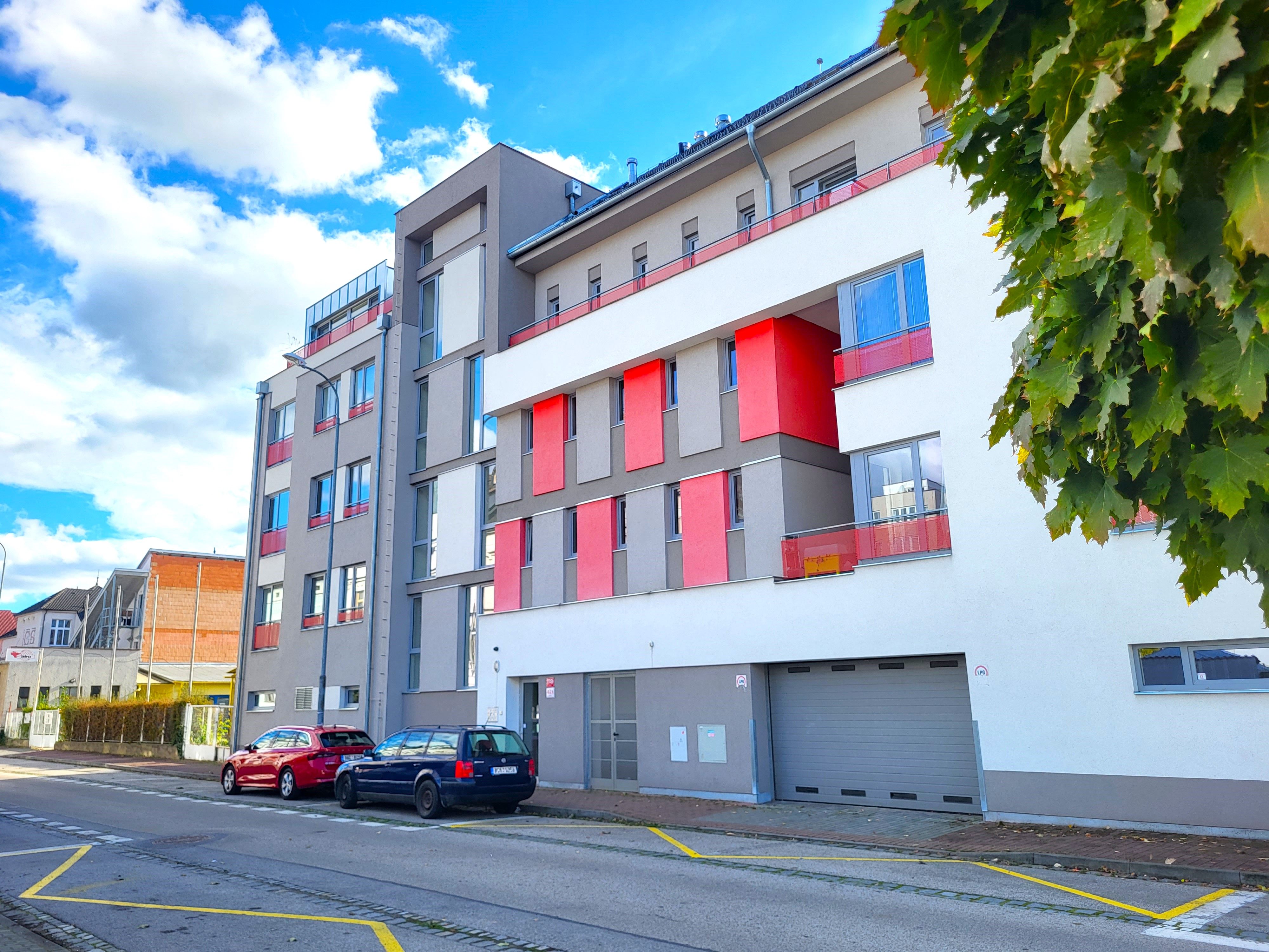 Moderní bytový dům s bílou a šedou fasádou a červenými balkony u ulice