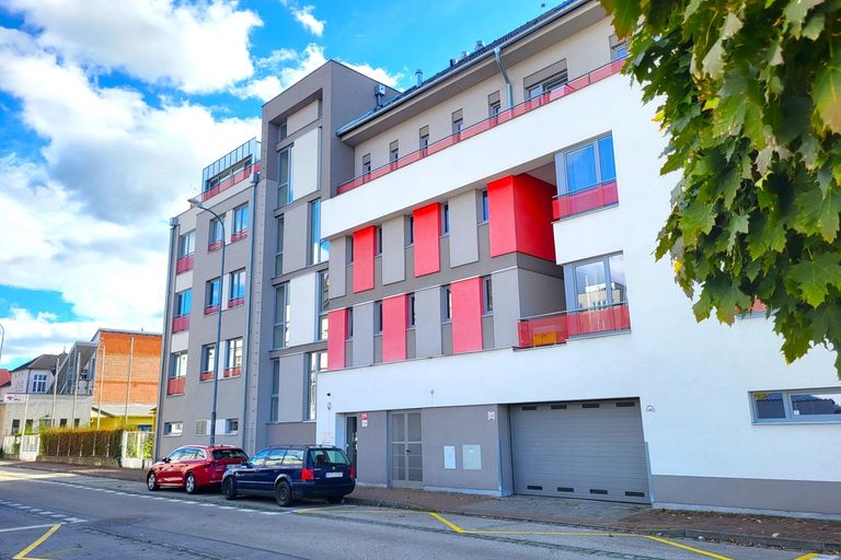 Moderní bytový dům s bílou a šedou fasádou a červenými balkony u ulice