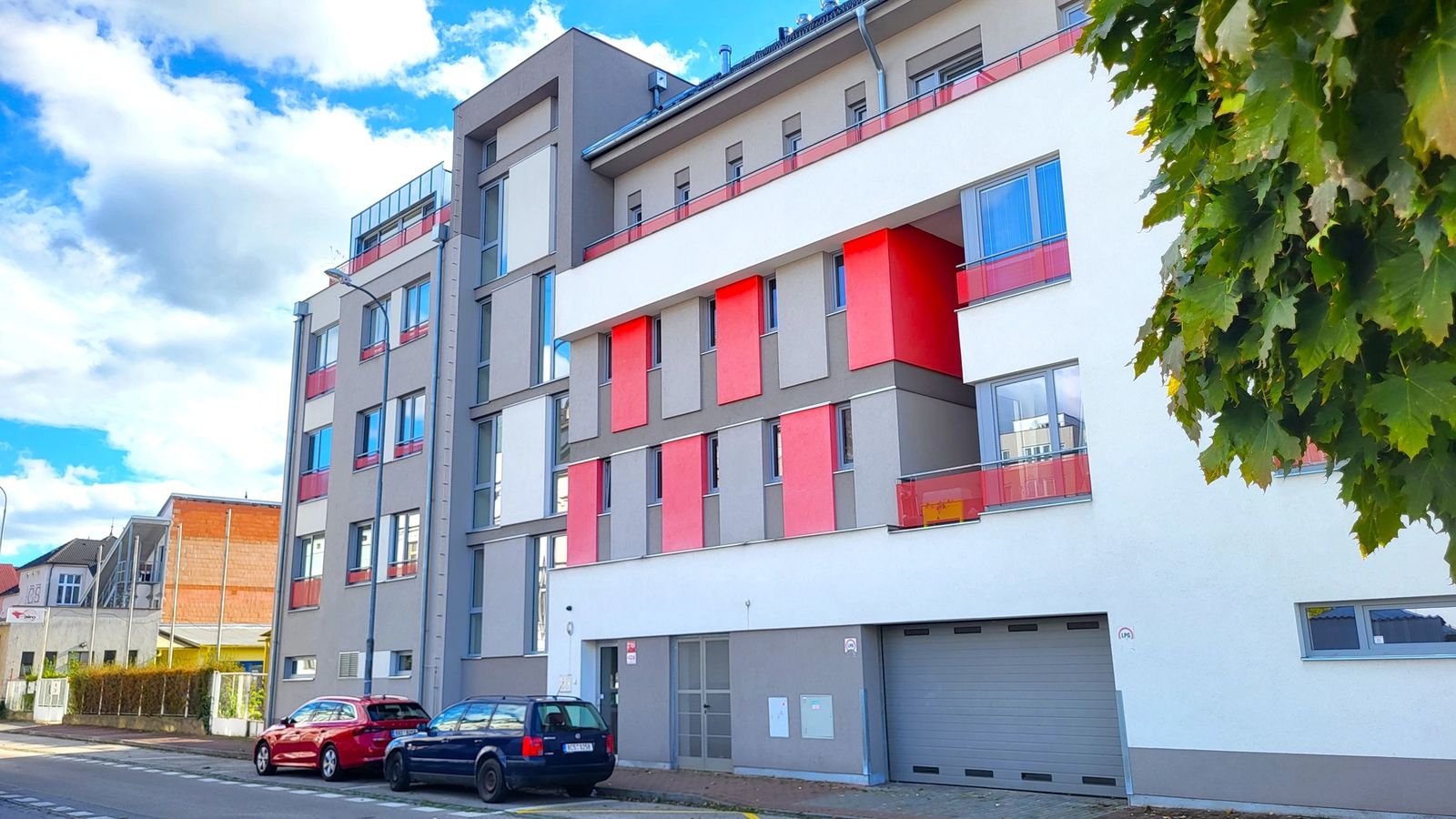 Moderní bytový dům s bílou a šedou fasádou a červenými balkony u ulice