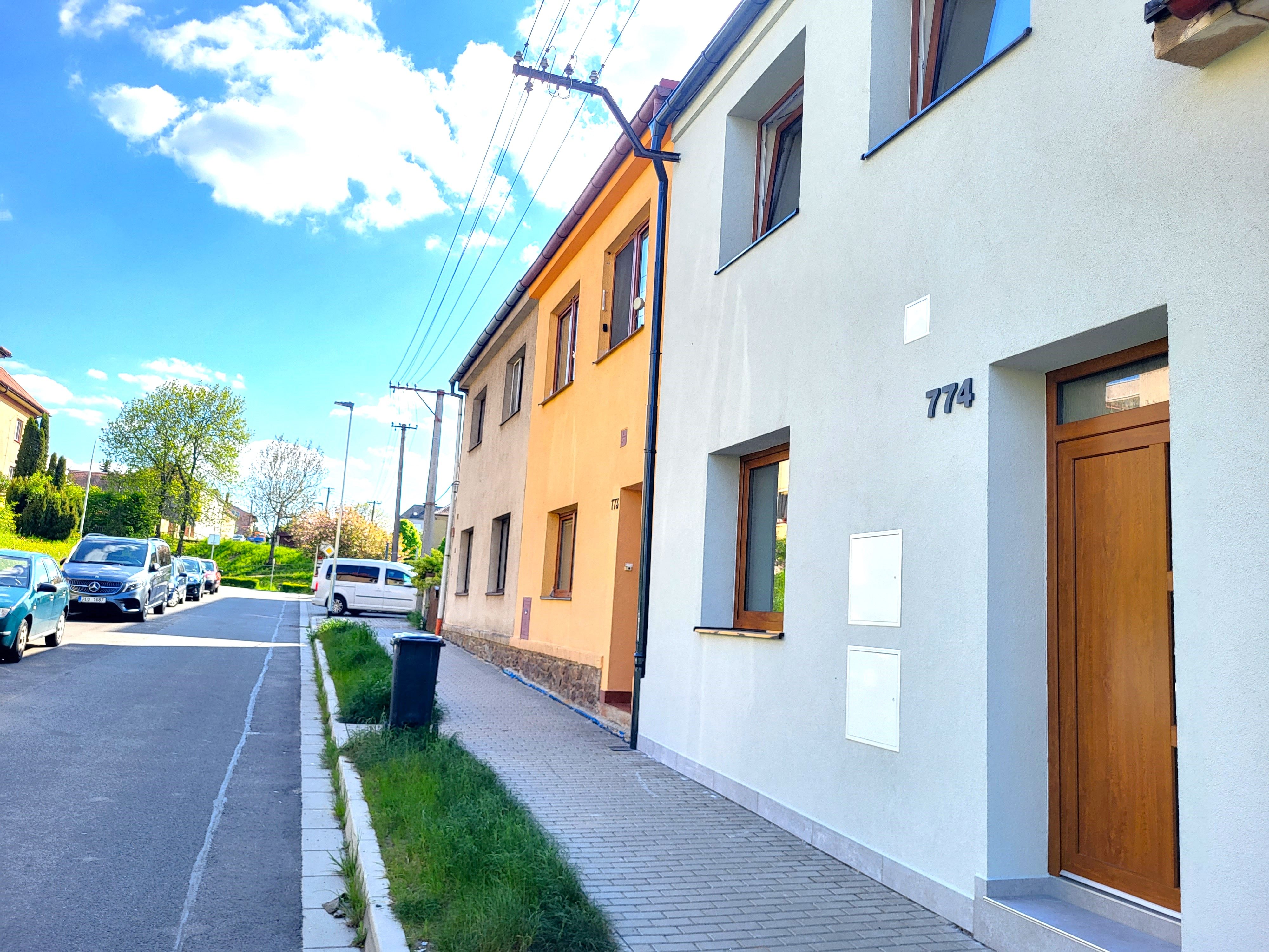 Řadový dům se světle šedou fasádou a dřevěnými vchodovými dveřmi u ulice