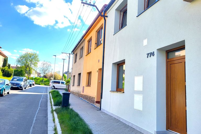 Řadový dům se světle šedou fasádou a dřevěnými vchodovými dveřmi u ulice