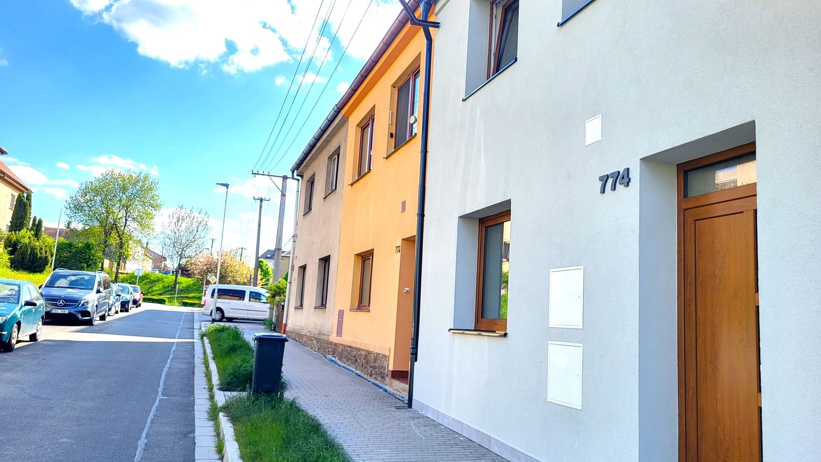 Řadový dům se světle šedou fasádou a dřevěnými vchodovými dveřmi u ulice