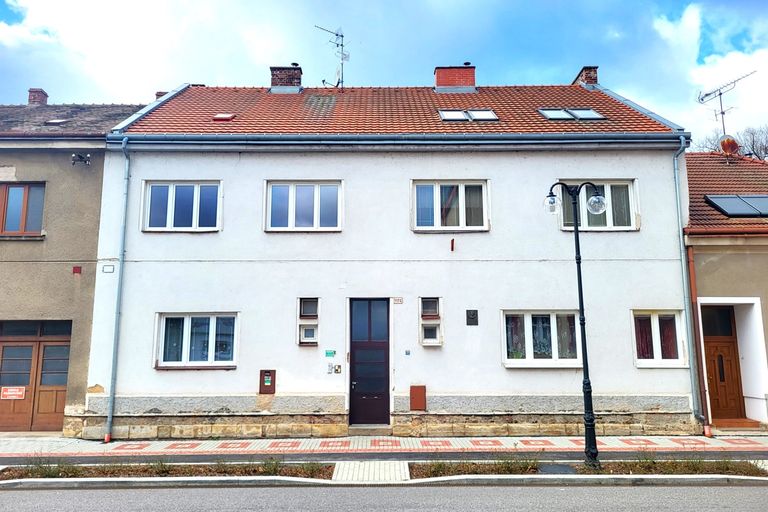 Bílý patrový řadový dům s červenou taškovou střechou u ulice s pouliční lampou