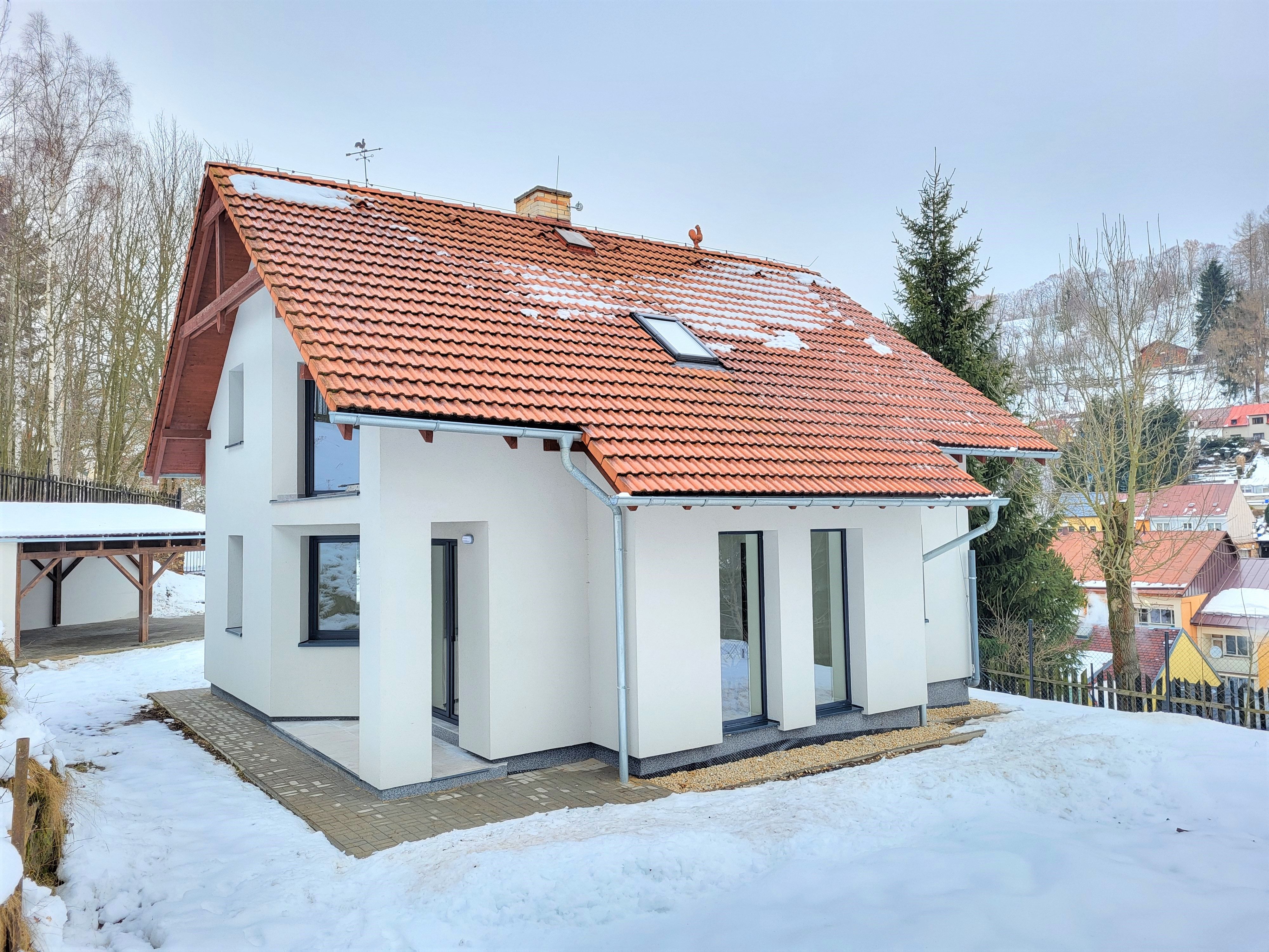 Bílý rodinný dům s oranžovou taškovou střechou v zimní zasněžené krajině