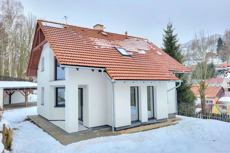 Bílý rodinný dům s oranžovou taškovou střechou v zimní zasněžené krajině