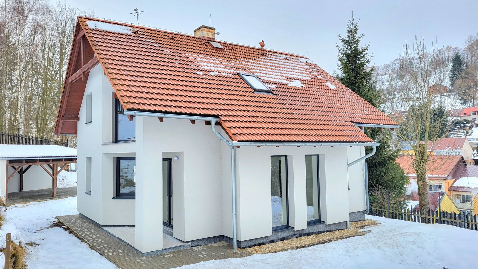 Bílý rodinný dům s oranžovou taškovou střechou v zimní zasněžené krajině