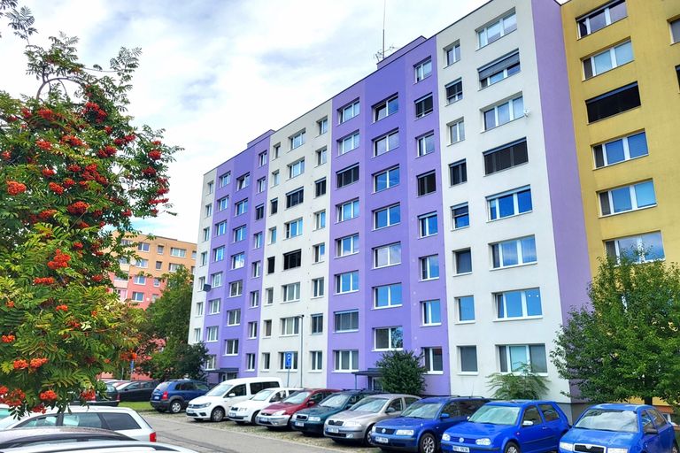 Panelový bytový dům s fialovou a bílou fasádou a parkovištěm s auty