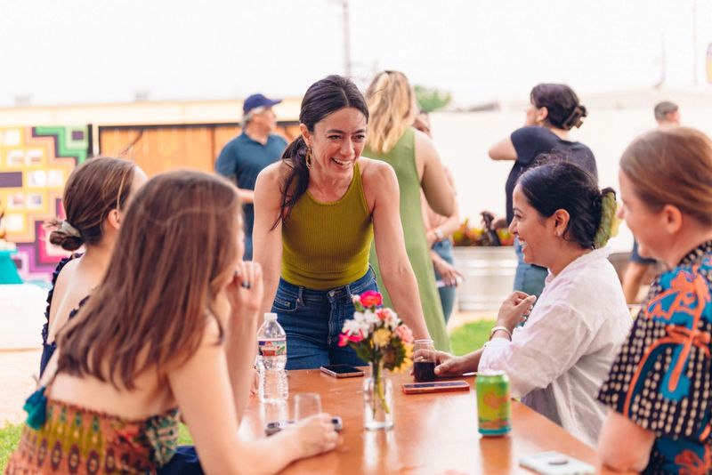 A group of people laugh together outside with drinks.