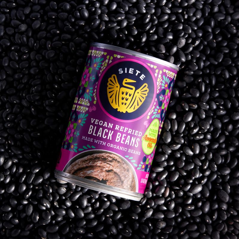 A can of Vegan Refried Black Beans on a background of black beans.