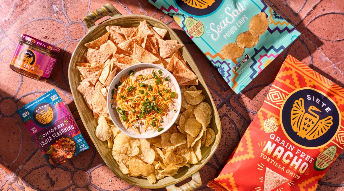 bags of siete tortilla and potato chips along with siete salsa and chicken fajita seasoning laying flat with a bowl of chips and beach dip
