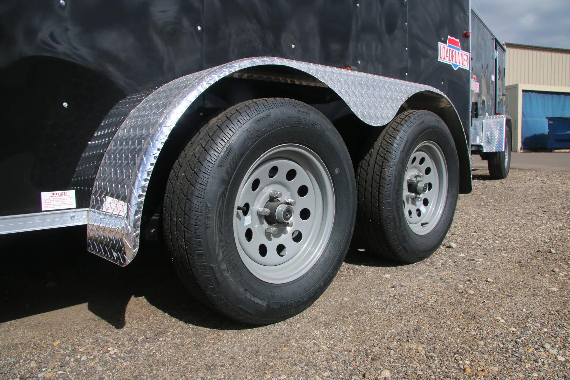 Close-up of a tandem-axle trailer's silver wheels and diamond-plate steel fender on a black enclosed cargo trailer