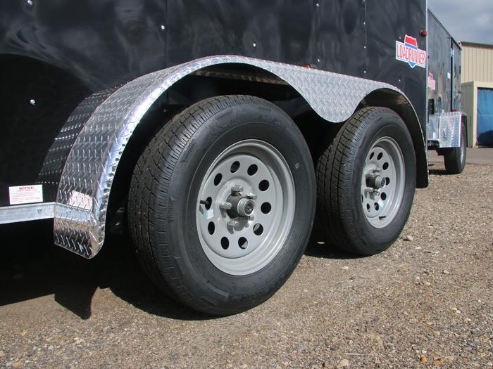 Close-up of a tandem-axle trailer's silver wheels and diamond-plate steel fender on a black enclosed cargo trailer