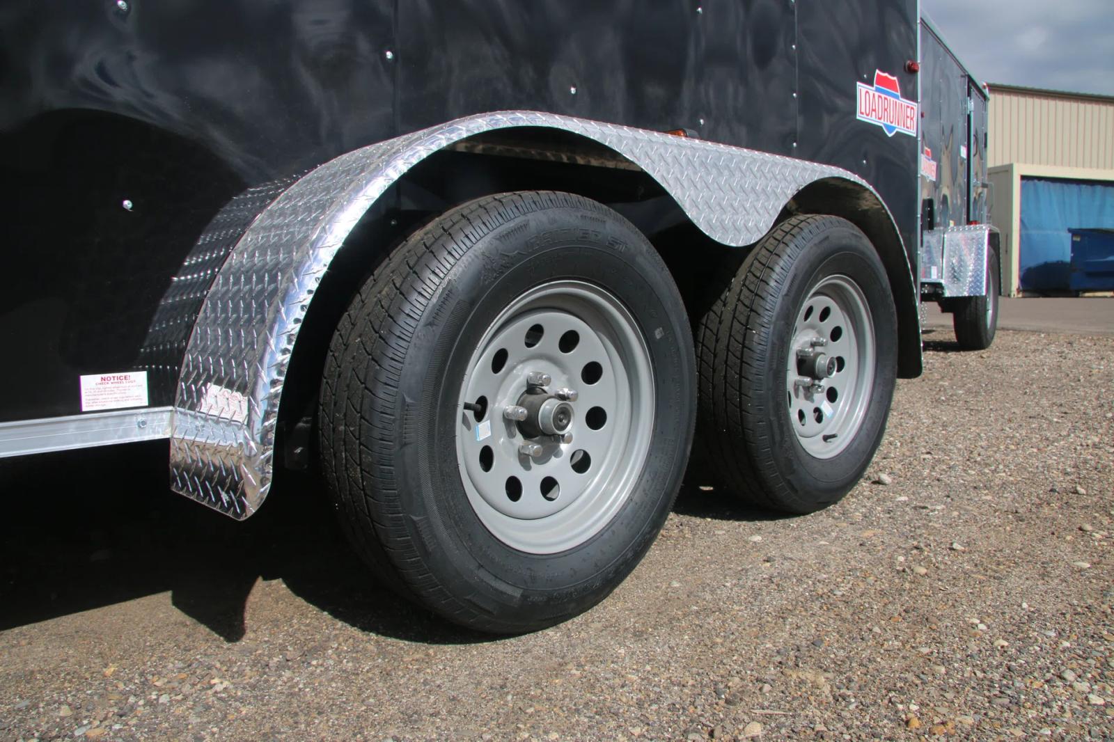 Close-up of a tandem-axle trailer's silver wheels and diamond-plate steel fender on a black enclosed cargo trailer