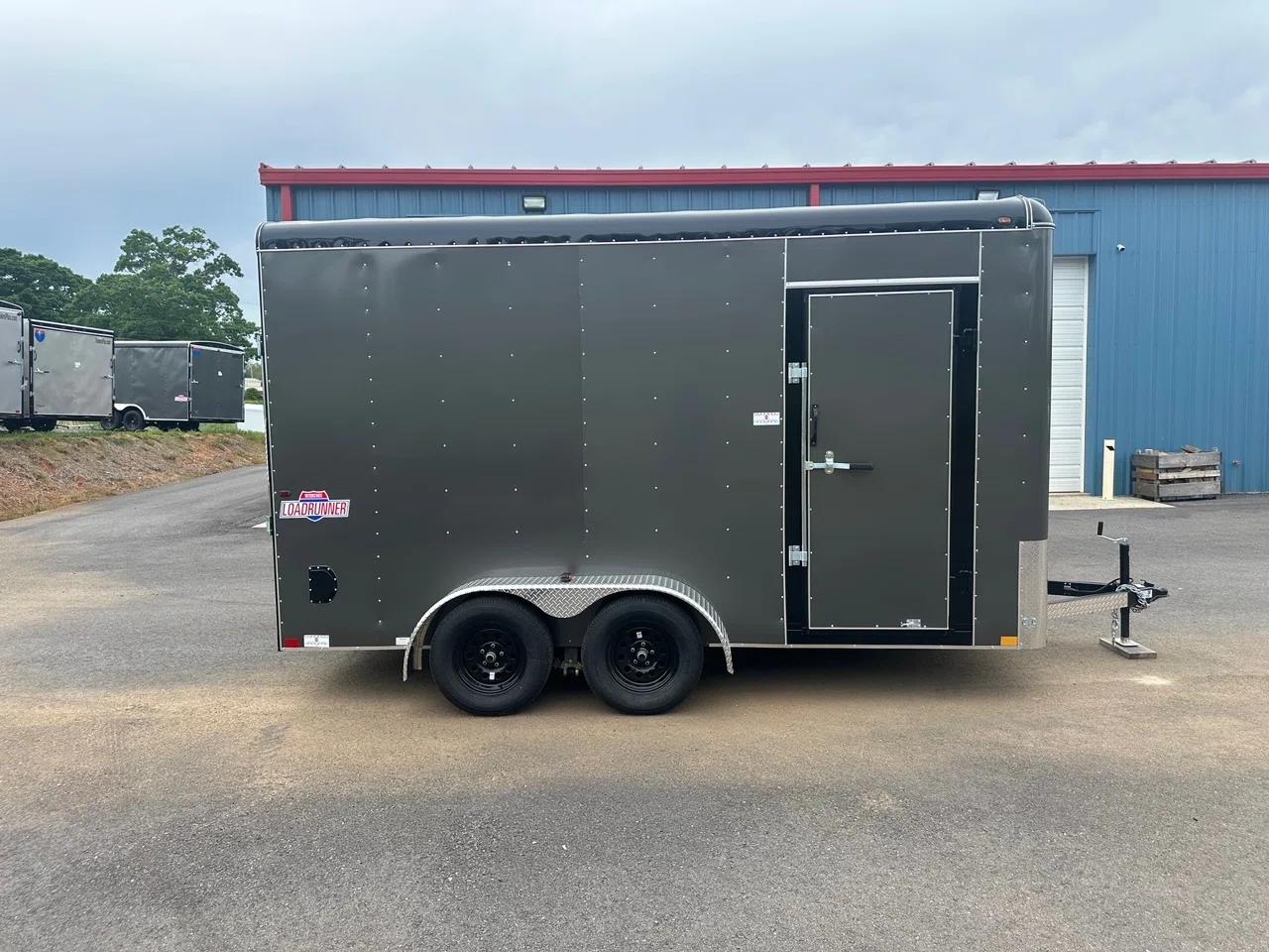 Charcoal Interstate Loadrunner enclosed cargo trailer parked at a paved lot in front of a red and blue steel warehouse