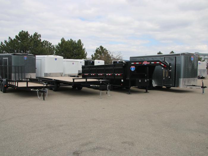 Lineup of a black utility, flatbed deckover, gooseneck dump, and charcoal enclosed cargo trailer with white cargo trailers behind on a TrailersPlus lot